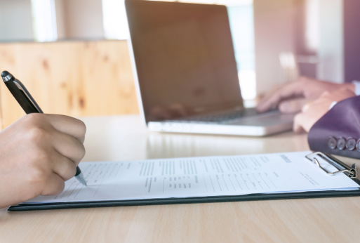 Employer reviewing a resumé, while another checks a laptop