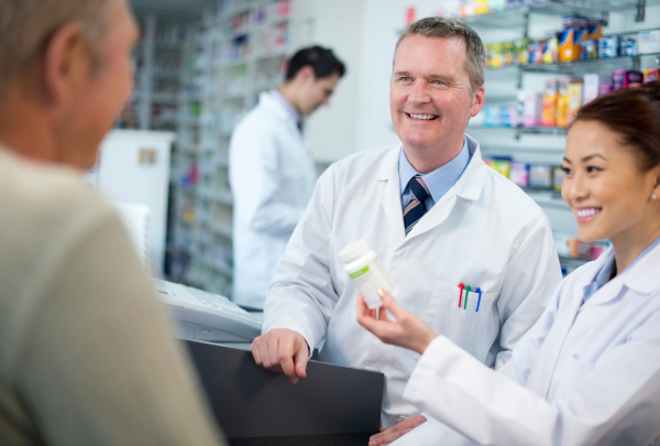 two pharmacists smiling while talking to a customer