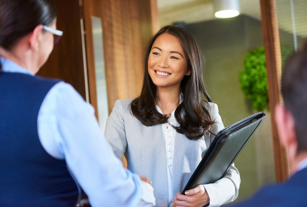 woman carrying folder, smiling and shaking another woman's hand