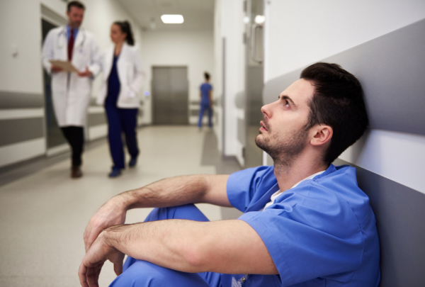 nurse sitting against wall looking stressed