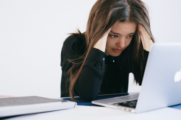 A woman sitting with her hands in her hair, looking stressed at a laptop screen.